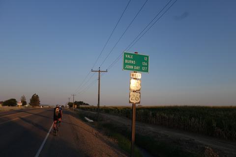 A highway milage sign under the powerlines and open sky